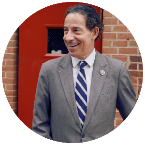 Rep. Raskin in grey suit with congressional pin with a backdrop of brick wall with red door